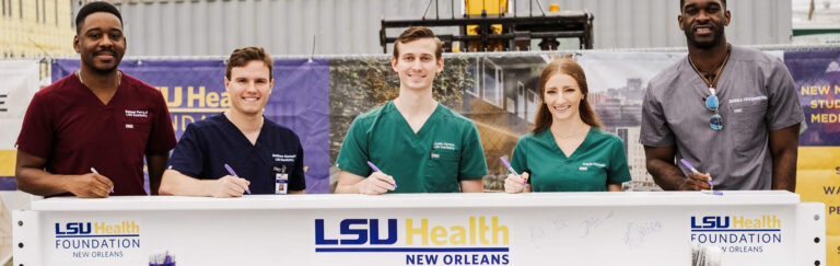 5 students signing a white construction beam that will be part of the new residences being built on the LSU Health campus